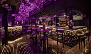Bar area of a dimly lit restaurant with an Asian theme and pink lights running across the ceiling.